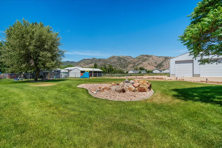 Expansive green lawn featuring a decorative rock garden, an adjacent white metal building with two garage doors, and distant mountain scenery