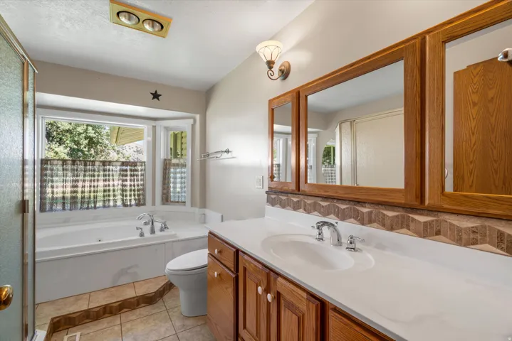 Bathroom featuring a spacious built-in tub with bay windows, a double vanity with ample counter space, built-in medicine cabinets with wood-finish frames, and tiled flooring with a decorative border