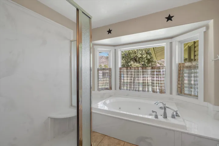Integrated jetted bathtub with a surrounding white countertop, complemented by a walk-in shower featuring a built-in bench