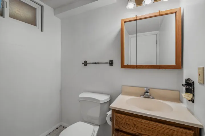 Compact bathroom featuring a corner vanity with integrated sink, wood-finish cabinetry, and a mirrored medicine cabinet