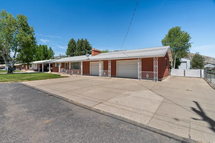 Brick exterior residence featuring two attached garage bays with white doors, a covered carport, and an expansive concrete driveway