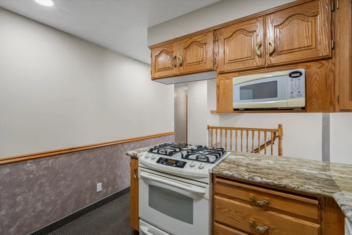 Kitchen featuring oak cabinetry, granite-finish countertops, built-in microwave, white gas range, and textured wall finish