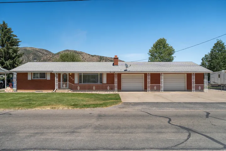 Ranch-style residence featuring a red brick exterior with white trim, a covered front porch with decorative railings, and a double-wide driveway leading to a two-car garage