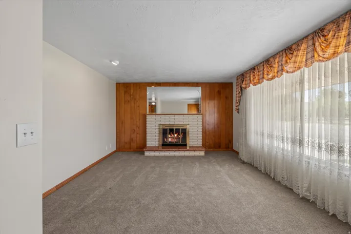 Carpeted living space with a brick fireplace and wood-paneled accent wall