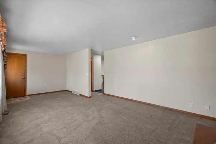 Carpeted living space featuring neutral wall tones, wood trim, and a textured ceiling