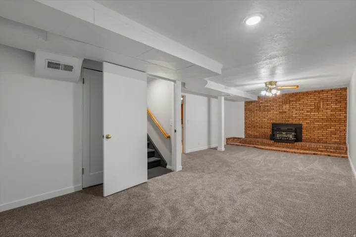 Spacious lower-level room featuring a brick fireplace with a raised hearth, light gray carpeting, and recessed lighting