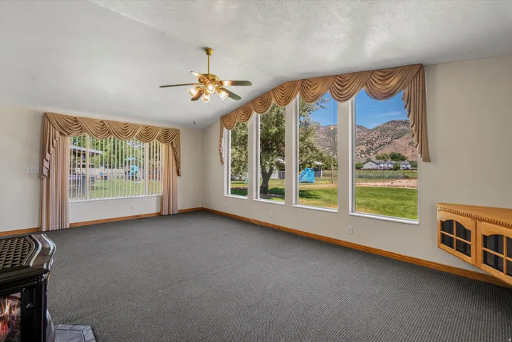 Spacious room featuring multiple large windows, wall-to-wall carpeting, a brass-finish ceiling fan with integrated lighting, and a built-in wooden cabinet