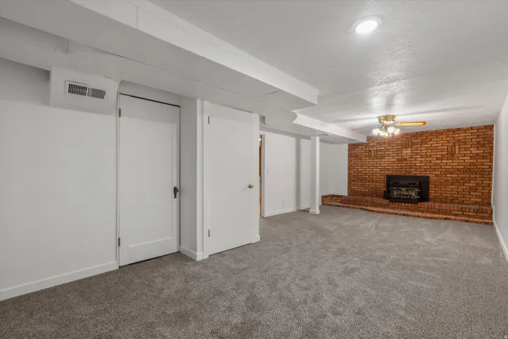 Spacious room featuring a brick fireplace with a raised hearth, light-colored carpeting, a ceiling fan, and recessed lighting