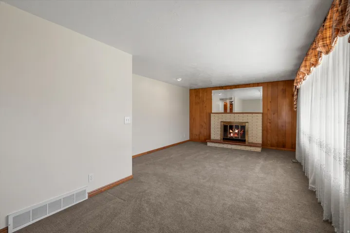 Central living area featuring a brick fireplace with a raised hearth, wood paneling, and a large window with sheer curtains
