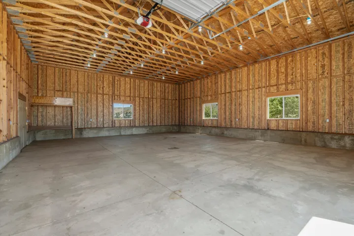 Spacious concrete-floored interior featuring exposed wood framing, multiple windows, and overhead lighting fixtures