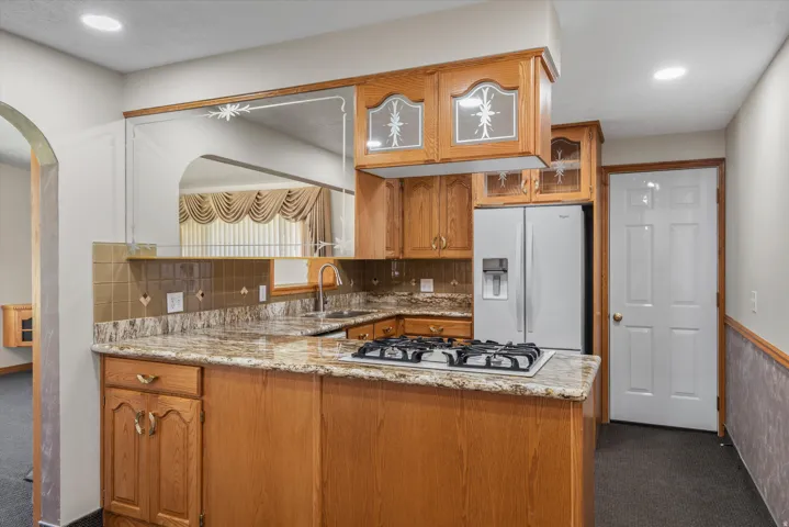 Kitchen featuring wood cabinetry, granite countertops, built-in gas range, stainless steel refrigerator, and tiled backsplash