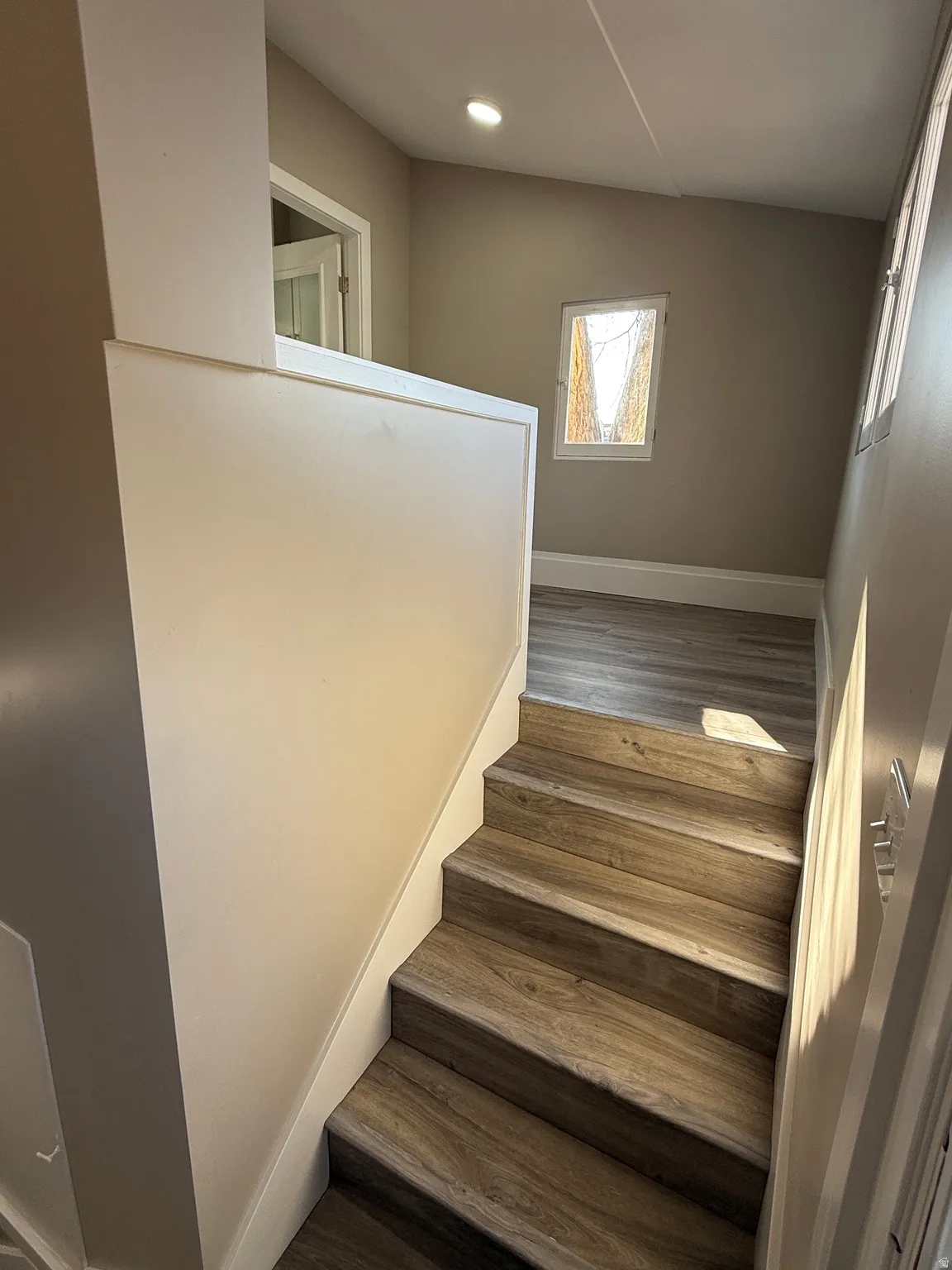 Staircase featuring wood-finish treads and risers, a painted half-wall, recessed ceiling lighting, and neutral wall tones
