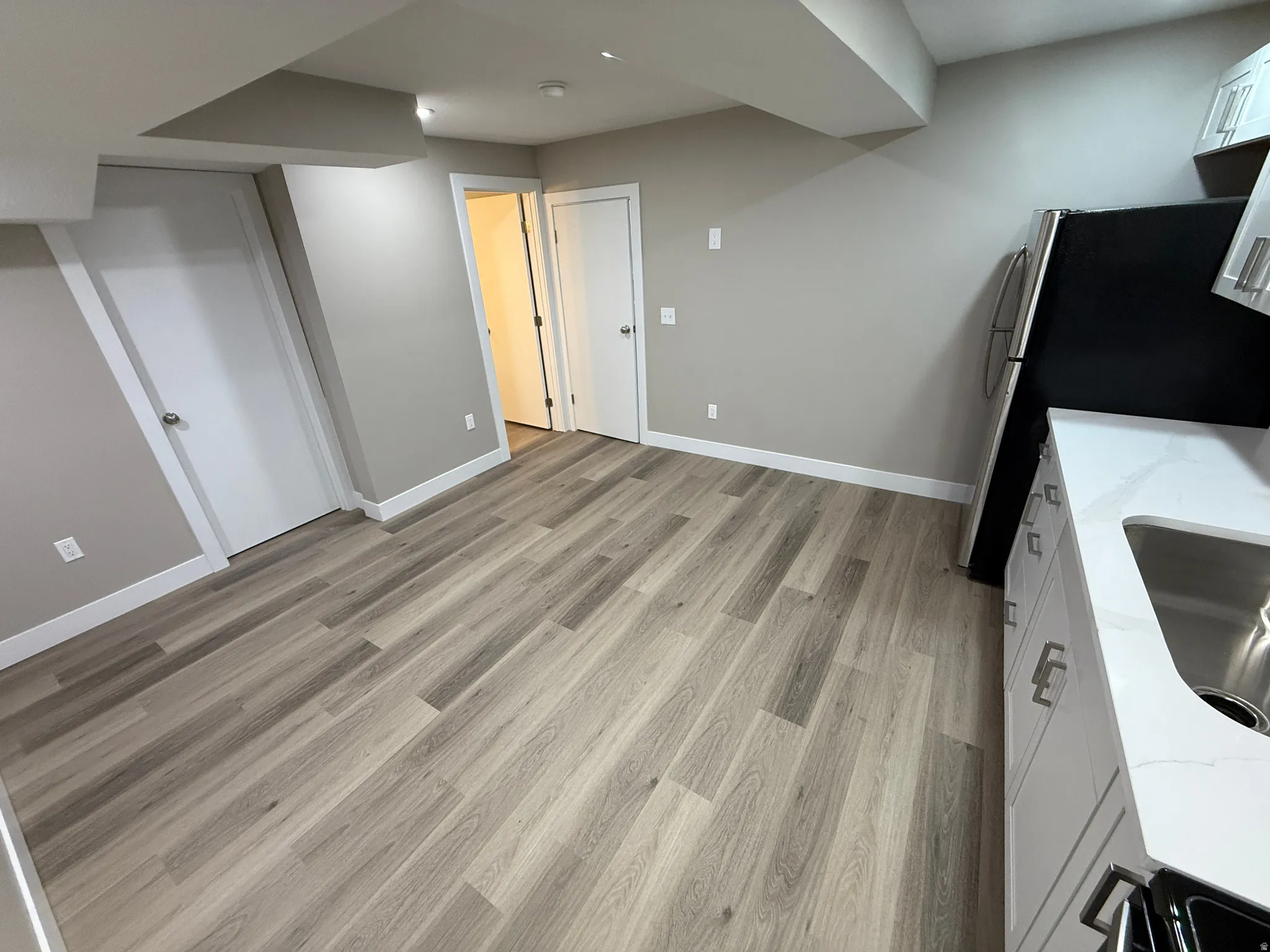 Open-concept space featuring wood-finish flooring, light gray walls, white baseboards, a kitchen area with white cabinetry, and stainless steel appliances
