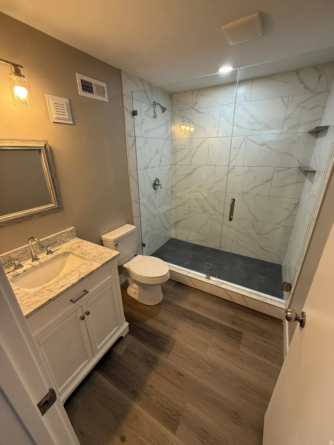 Bathroom featuring a glass-enclosed shower with large format marble-look wall tiling and dark tile shower pan