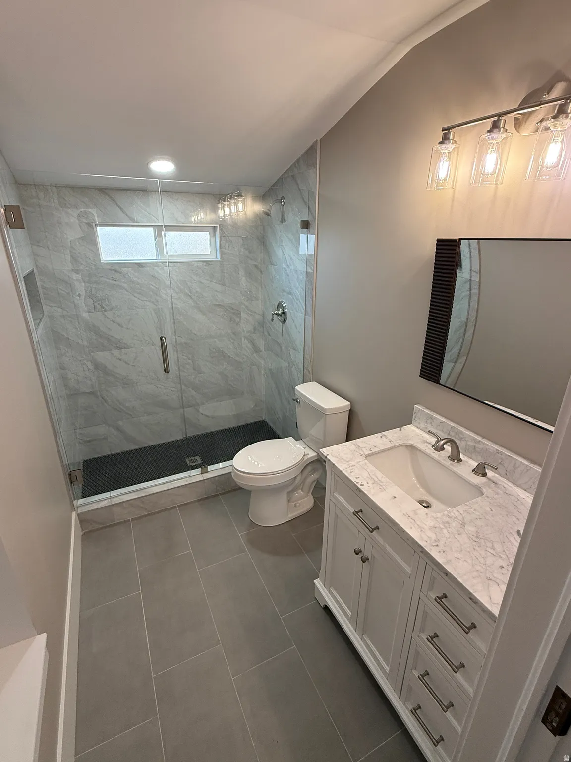Modern bathroom featuring a glass-enclosed shower with gray tiled walls and a black shower pan