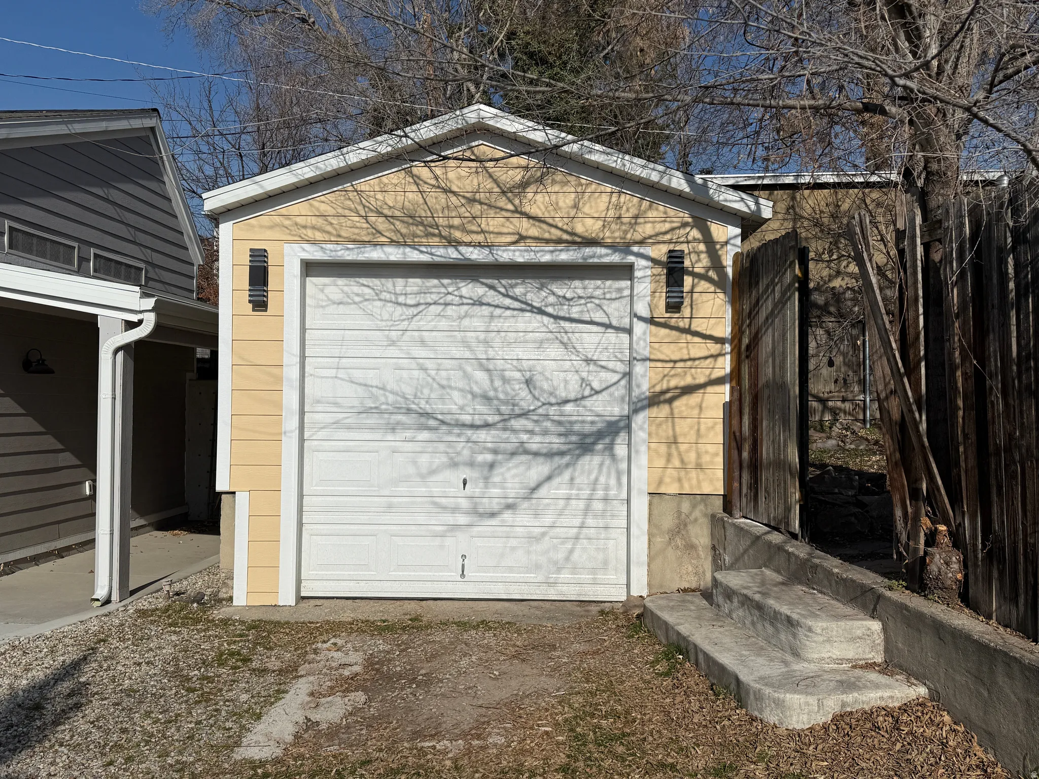Detached garage featuring a white panel door, yellow horizontal siding, and two exterior sconce lights