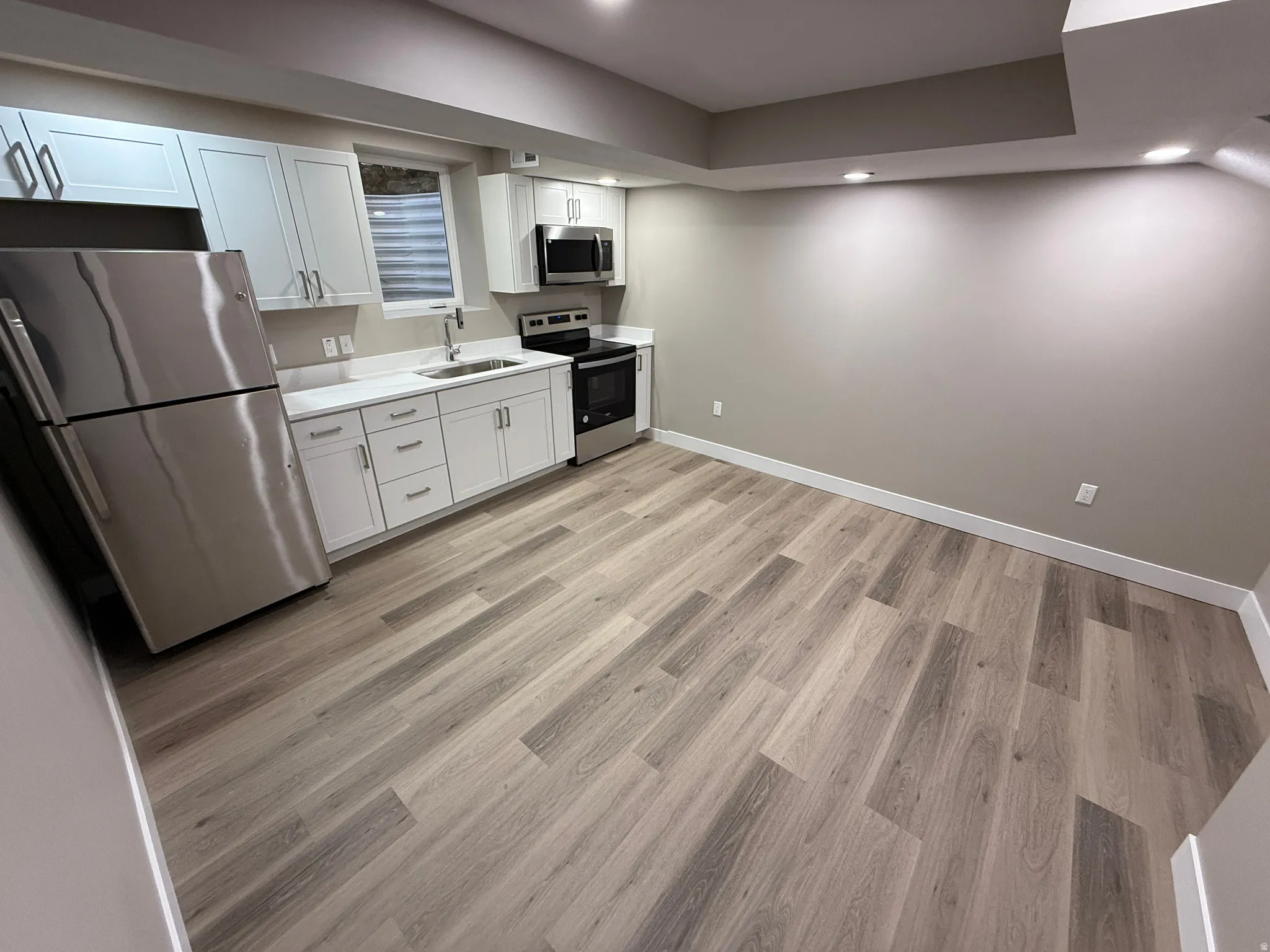Contemporary kitchen space featuring wood-finish flooring, white cabinetry, stainless steel appliances, and recessed lighting