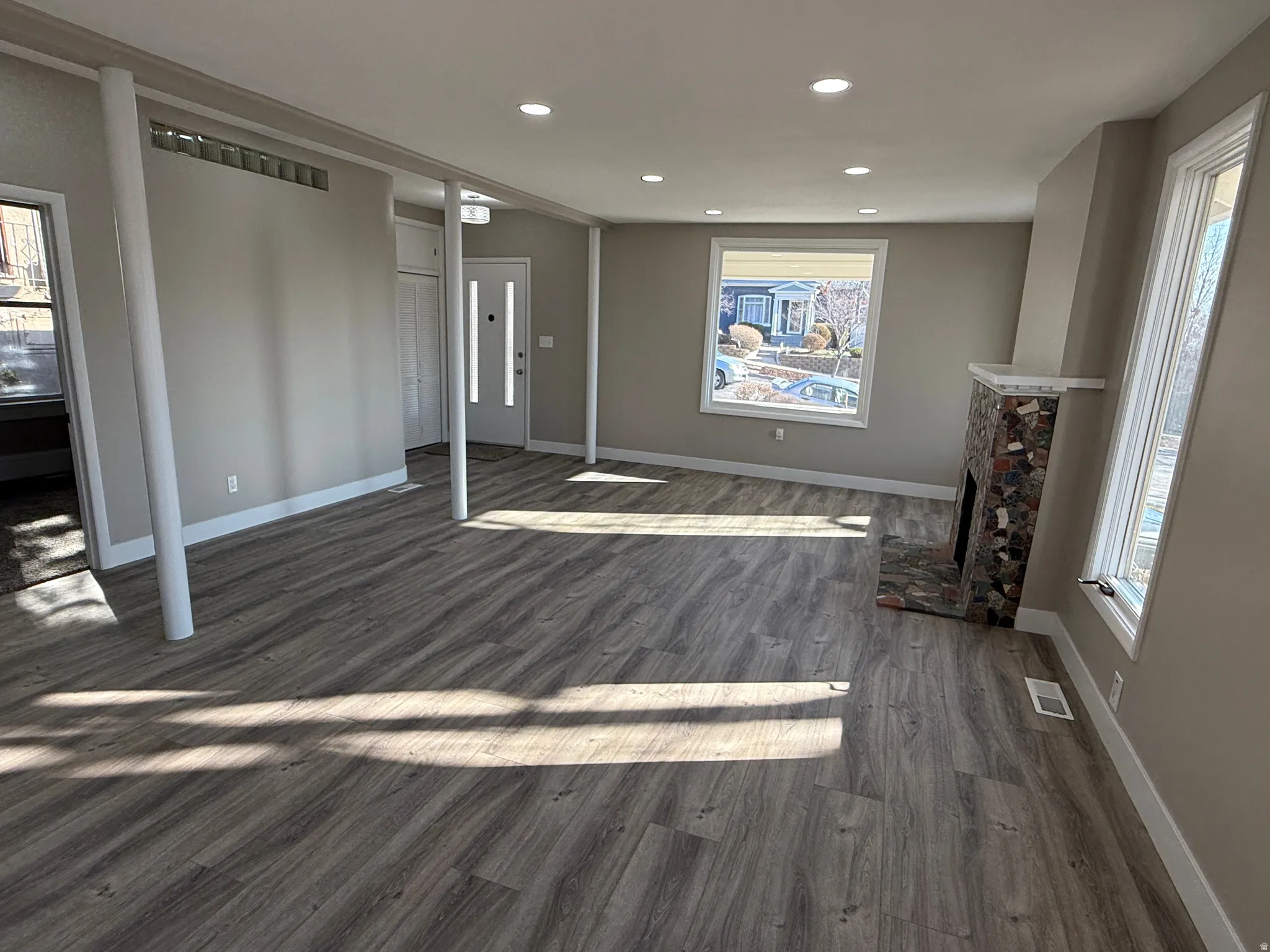 Spacious living area featuring wood-finish flooring, recessed lighting, and a stone-clad fireplace