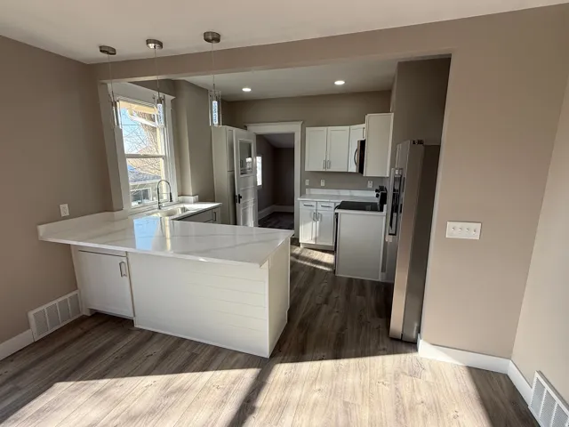 Kitchen featuring a peninsula with waterfall countertop, pendant lighting, wood-finish flooring, white cabinetry, and stainless steel appliances