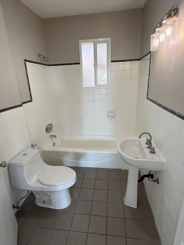 Bathroom featuring white subway tile walls with black trim, a full bathtub with shower, a contemporary pedestal sink, a modern toilet, and a vanity light fixture