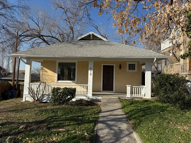 Charming bungalow featuring a covered front porch with white columns and railings, a light yellow stucco exterior, and a dark wood entry door