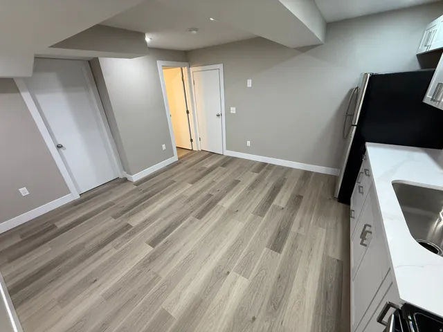 Open-concept space featuring wood-finish flooring, light gray walls, white baseboards, a kitchen area with white cabinetry, and stainless steel appliances