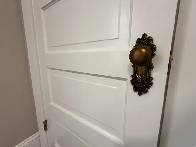 White paneled door featuring an ornate bronze door knob and escutcheon plate