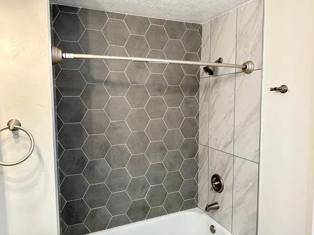 Bathtub and shower combination featuring hexagonal dark gray tile and large format light gray marbled tile surrounds