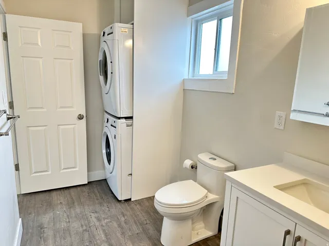 Bathroom featuring wood-finish flooring, a white vanity with an integrated sink, a modern toilet, and a window