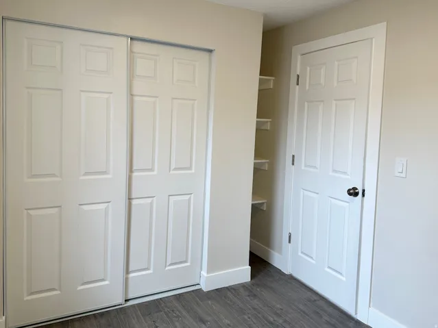 White six-panel sliding closet doors, wood-finish flooring, white baseboards, and built-in shelving