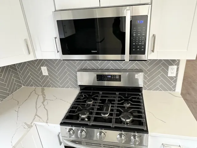Stainless steel range with coordinating overhead microwave, set against a grey herringbone tile backsplash