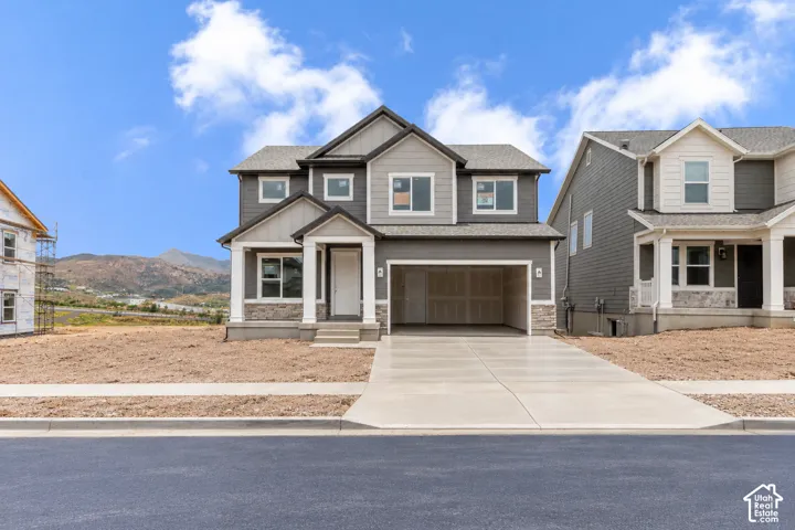 Two-story exterior featuring composite siding, stone veneer accents, a covered front porch with square columns, an attached two-car garage, and mountain backdrop