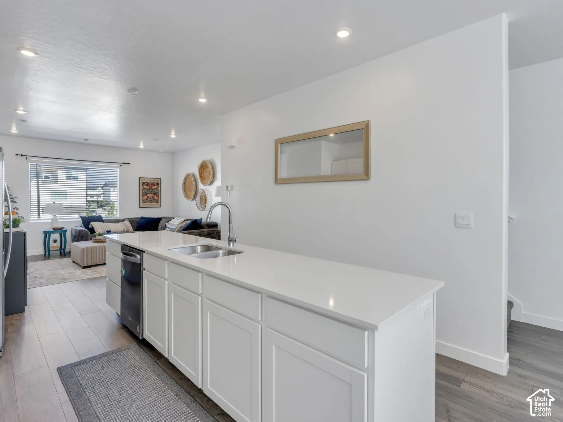 Kitchen island featuring a single basin stainless steel sink, a chrome gooseneck faucet, white shaker-style cabinetry, and a black dishwasher