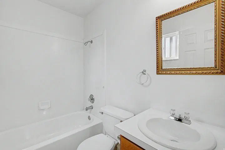 Bathroom featuring a white bathtub with shower, white toilet, and a vanity with an integrated sink
