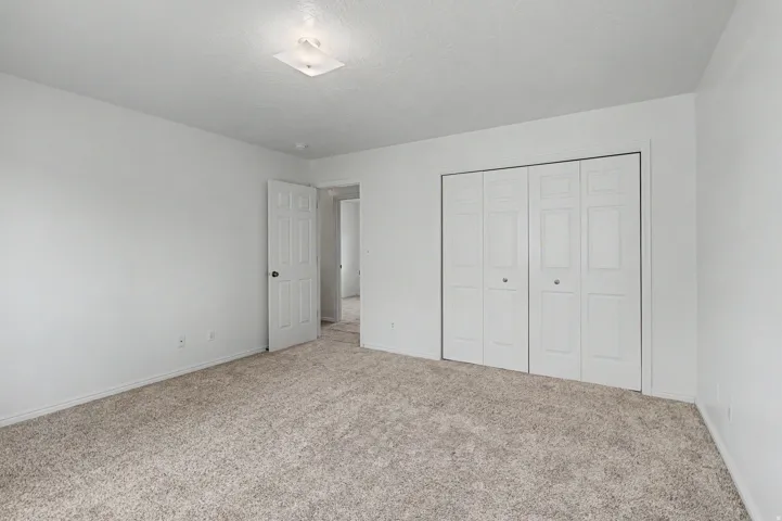Spacious room featuring neutral carpeting, crisp white walls, and a white bi-fold closet with circular hardware