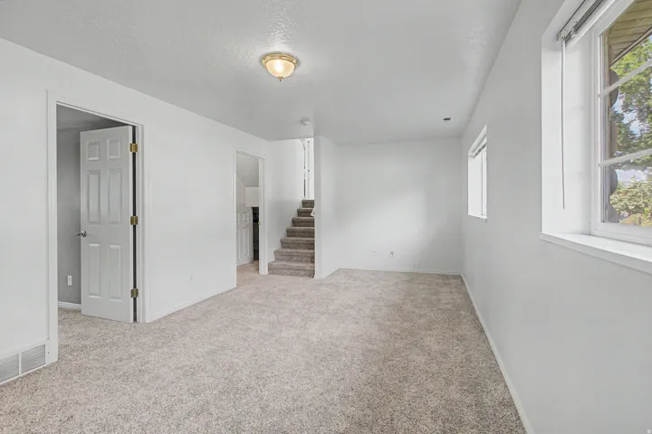 Spacious room featuring light-colored carpeting, white painted walls, and multiple windows allowing for natural light