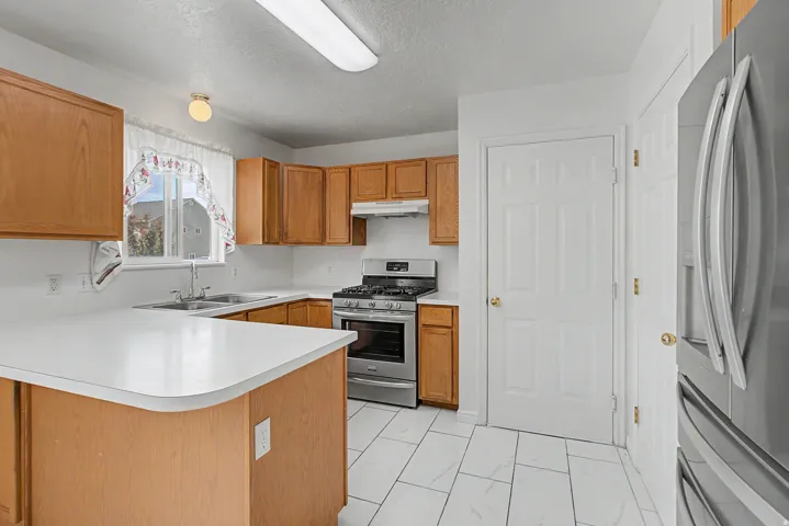 Kitchen featuring wood cabinetry, white countertops, stainless steel appliances, and white tile flooring