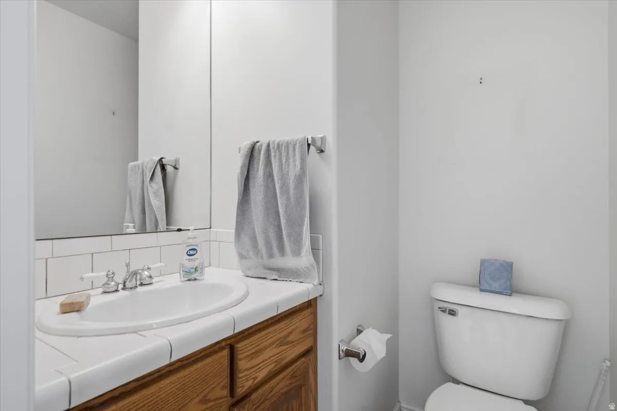 Bathroom vanity featuring a white oval sink with chrome faucet, white tiled countertop, and wood-finish cabinetry