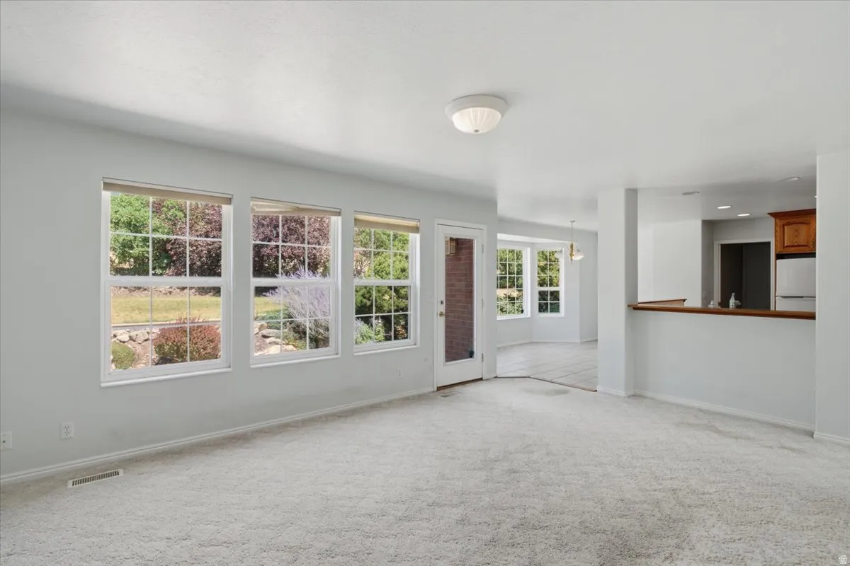 Spacious living area featuring light-toned carpeting and multiple windows offering abundant illumination
