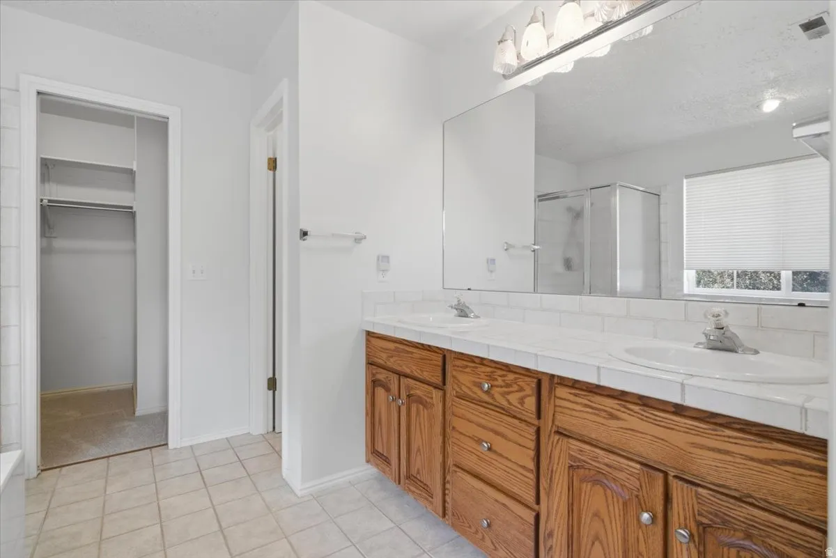 Bathroom featuring a double vanity with wood cabinetry, a tiled countertop, and a large mirror