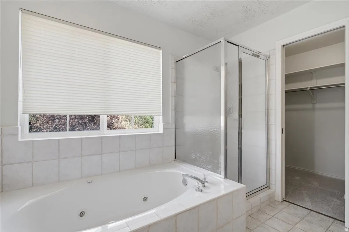 Spa-like bathroom with a jetted soaking tub, white tiled surround, and a glass-enclosed shower