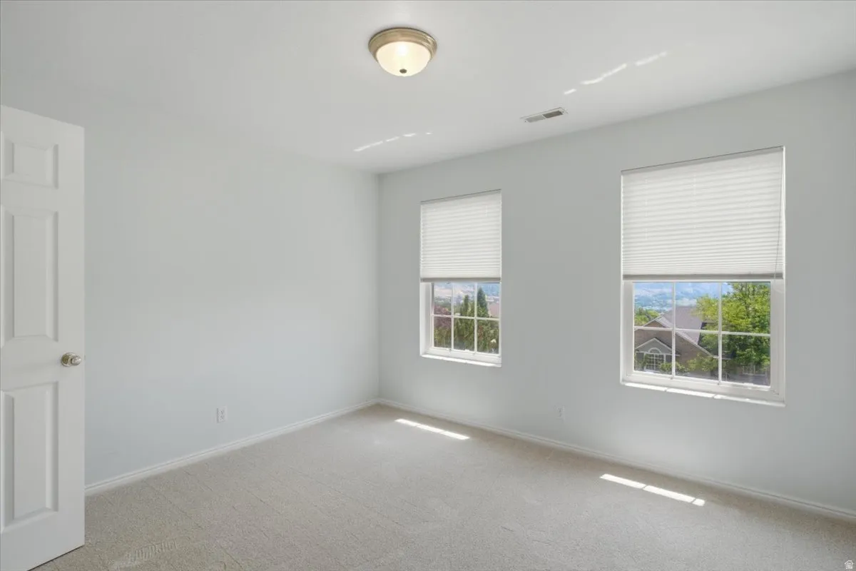 Neutral-toned carpeted interior space featuring two windows with horizontal blinds