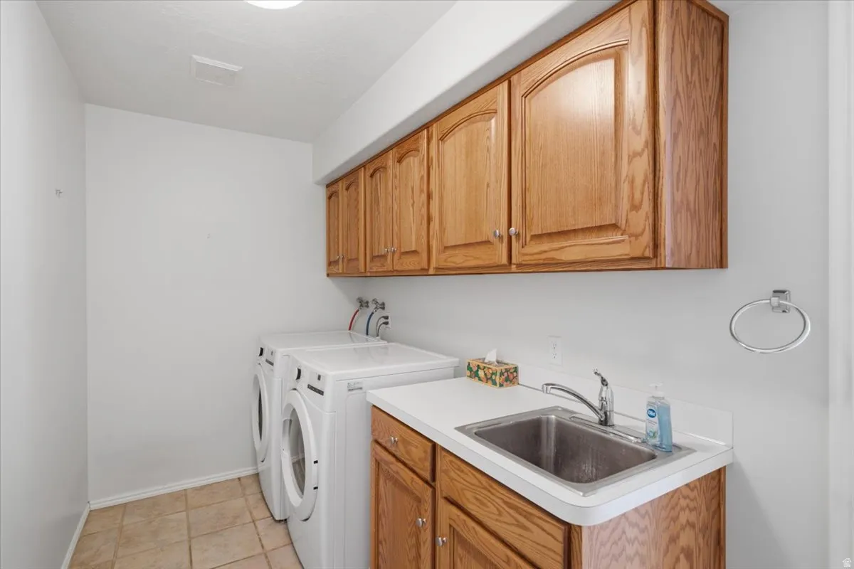 Laundry area featuring wood cabinetry, a utility sink with a stainless steel faucet, and tile flooring