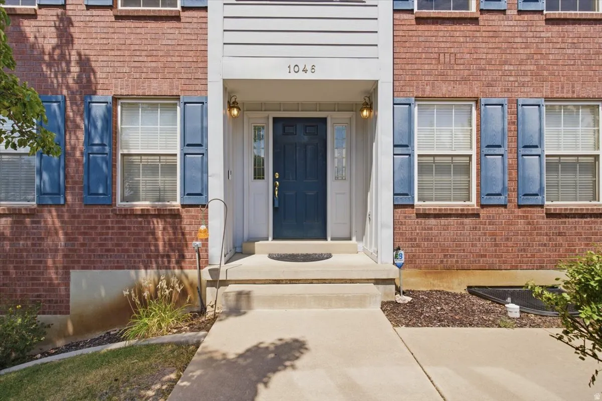 Brick exterior with blue shutters, a concrete walkway, and a covered entry