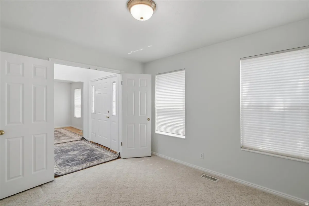 Carpeted room with double entry doors and two windows featuring horizontal blinds