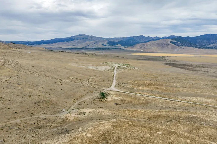 Expansive undeveloped land with a dirt road, offering a natural landscape with distant mountains under a cloudy sky