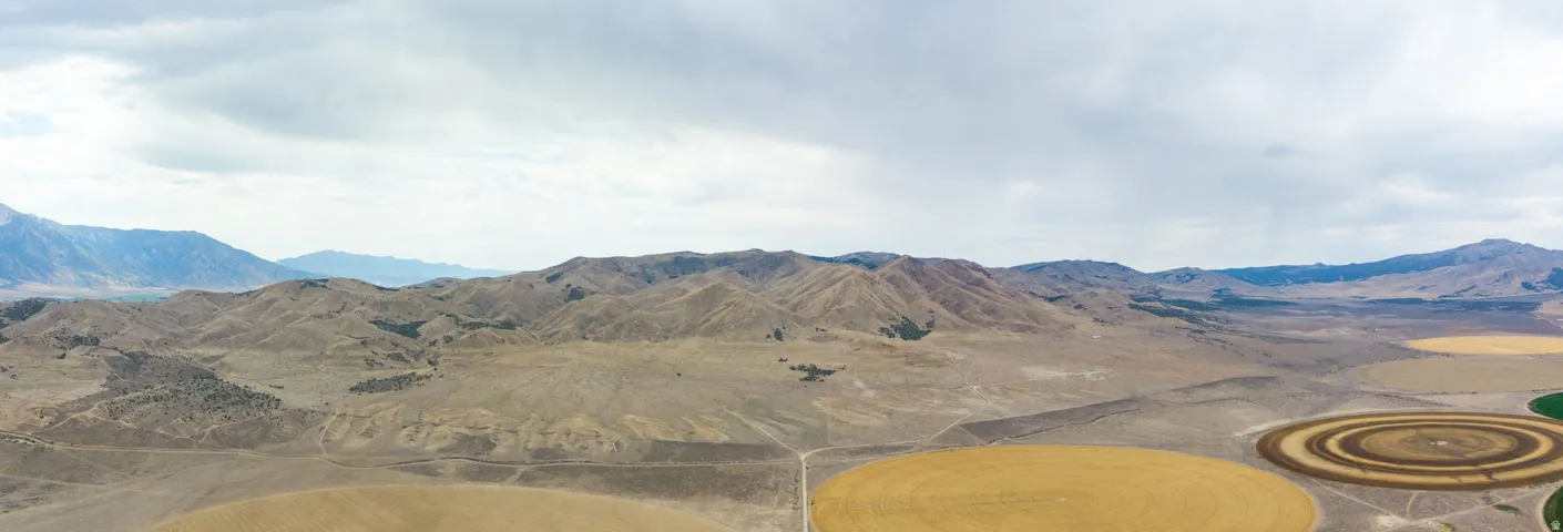 Expansive rural landscape featuring circular fields, mountainous terrain, and a winding dirt road