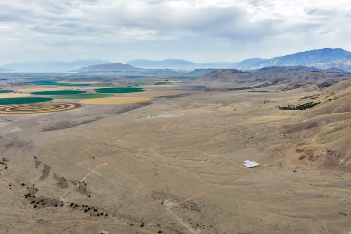 Expansive land parcel featuring a visible white-roofed structure, surrounded by natural desert terrain and distant mountains