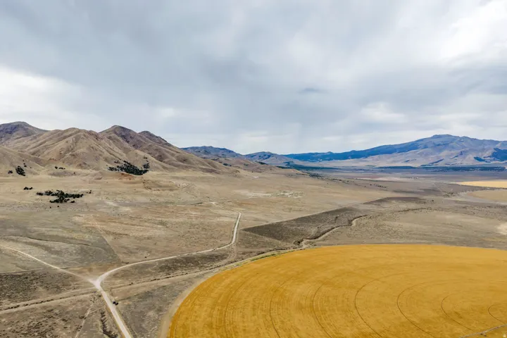 Expansive rural landscape featuring a circular field, unpaved roads, and distant mountains