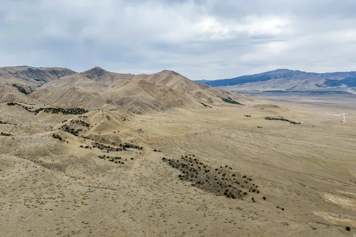 Expansive desert landscape featuring rolling hills and distant mountains under a cloudy sky